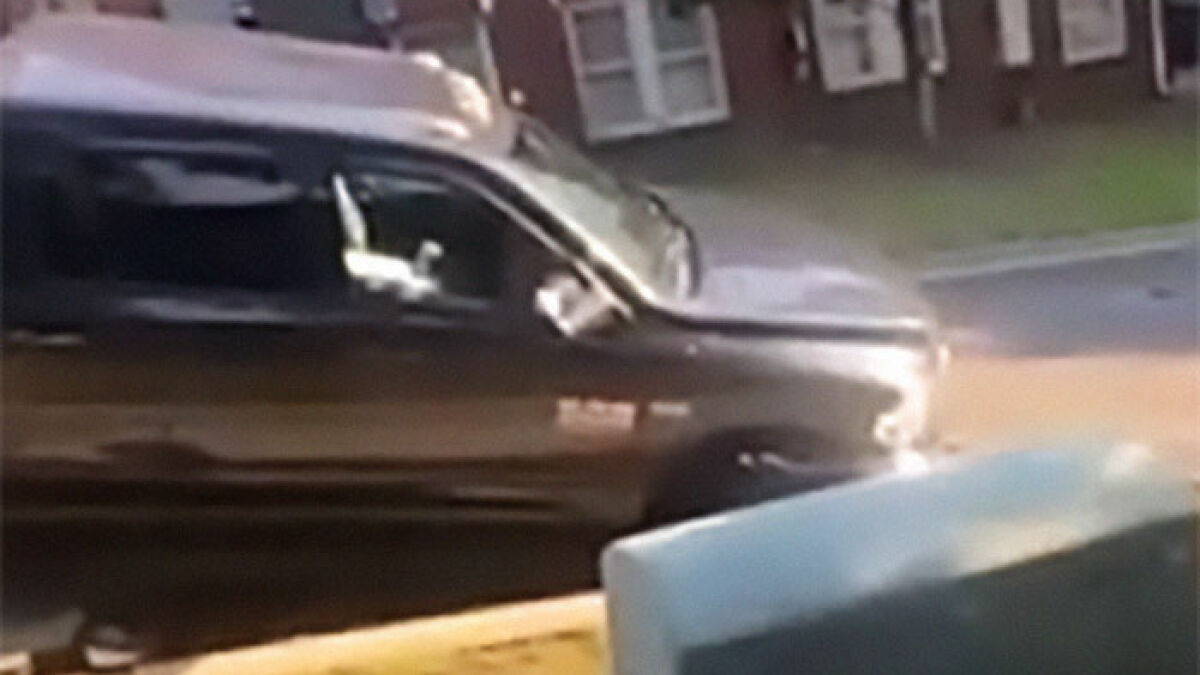 A black truck stopping near a sinkhole as a man signals a warning about the danger on a residential street.