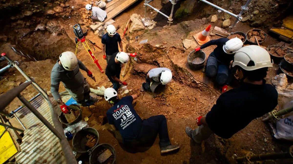 Archaeologists excavating prehistoric site wearing helmets and gloves uncovering evidence of ancestors eating toddlers like prey