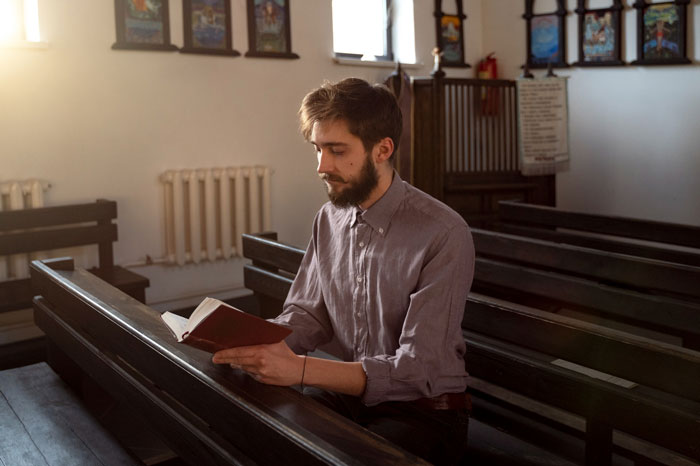 Man sitting in church pew reading a book, representing religious beliefs linked to feminine hygiene waste bins issue. Man sitting in church pew reading a book, representing religious beliefs linked to feminine hygiene waste bins issue.