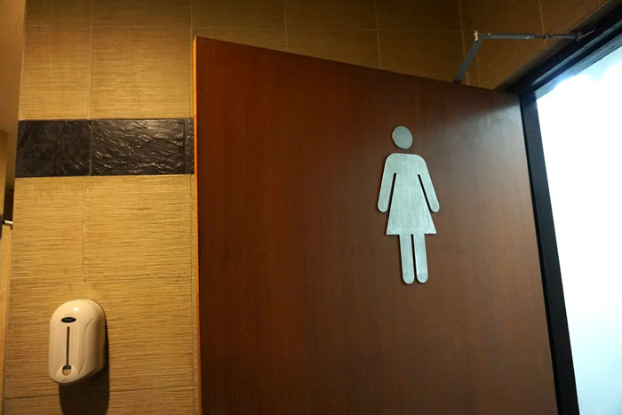 Women’s restroom door with hygiene waste bin inside, highlighting custodian’s refusal to empty bins due to religion. Women’s restroom door with hygiene waste bin inside, highlighting custodian’s refusal to empty bins due to religion.