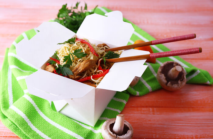Takeout box with noodles, chicken, and vegetables with chopsticks on a green towel, illustrating weirdest calls first responders.