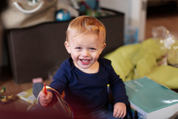 Smiling toddler playing indoors surrounded by books and toys, illustrating weirdest calls first responders found themselves on.