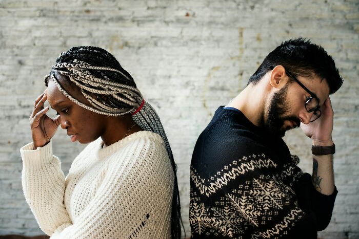Couple sharing reasons not divorced, sitting back to back looking thoughtful and stressed indoors against a brick wall.