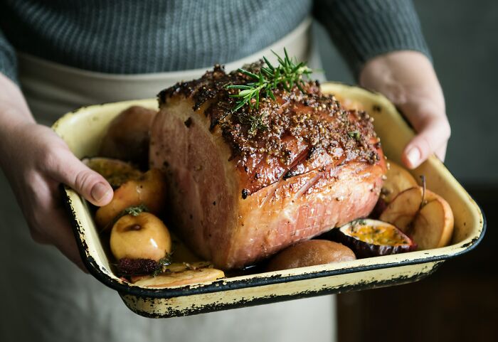 Person holding a tray with a roasted ham garnished with herbs and cooked fruits, illustrating common religious myths.