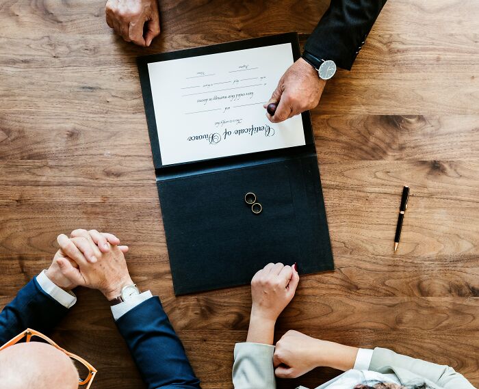 Couple sitting at a wooden table with a certificate and wedding rings while people share reasons not divorced