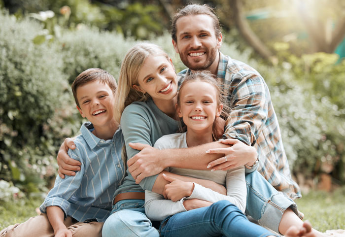 Smiling family outdoors with dad, daughter, stepmom, and son embracing, highlighting blended family dynamics. Smiling family outdoors with dad, daughter, stepmom, and son embracing, highlighting blended family dynamics.