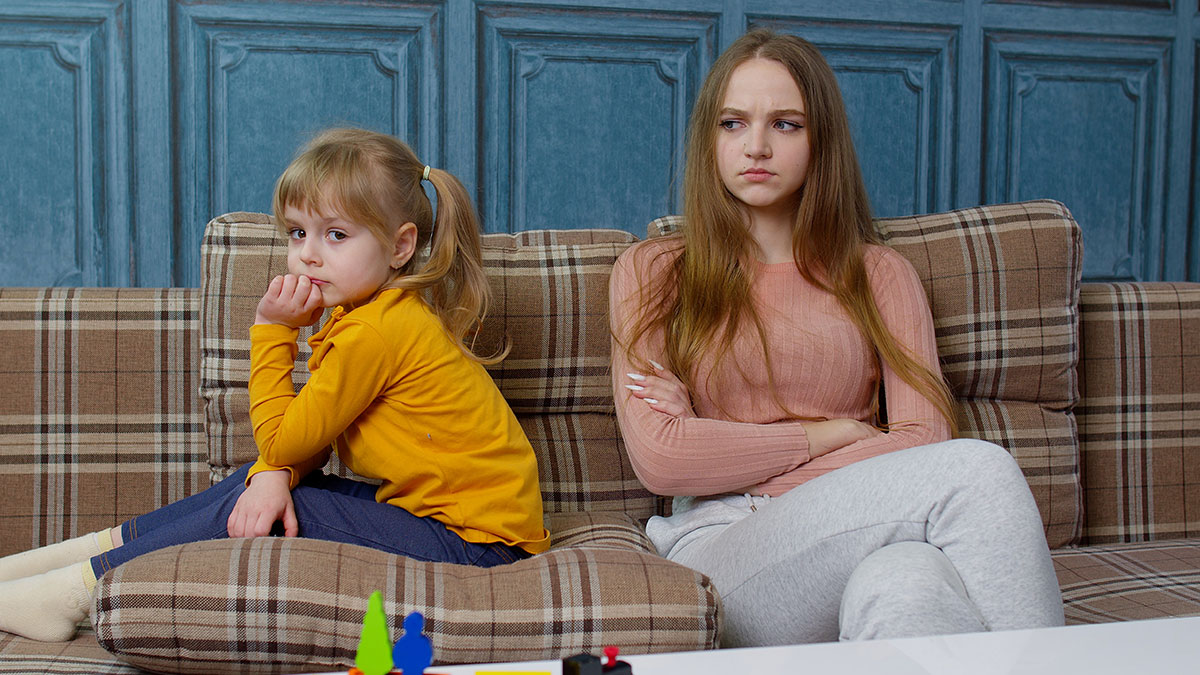 Young daughter and stepmom sitting apart on a couch, showing tension in family dynamics and stepmom acceptance issues.
