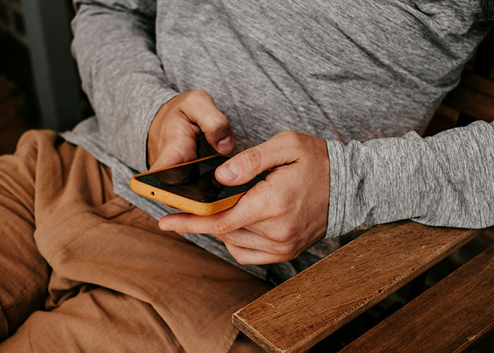 Man in gray shirt and brown pants holding a smartphone, representing a dad concerned about 8-year-old spending the night. Man in gray shirt and brown pants holding a smartphone, representing a dad concerned about 8-year-old spending the night.