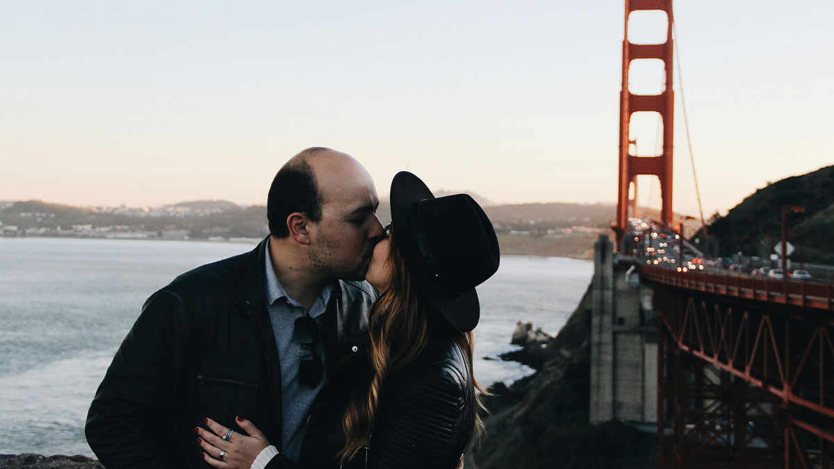 Couple kissing near Golden Gate Bridge at sunset, illustrating themes of manipulation and trust in relationships.