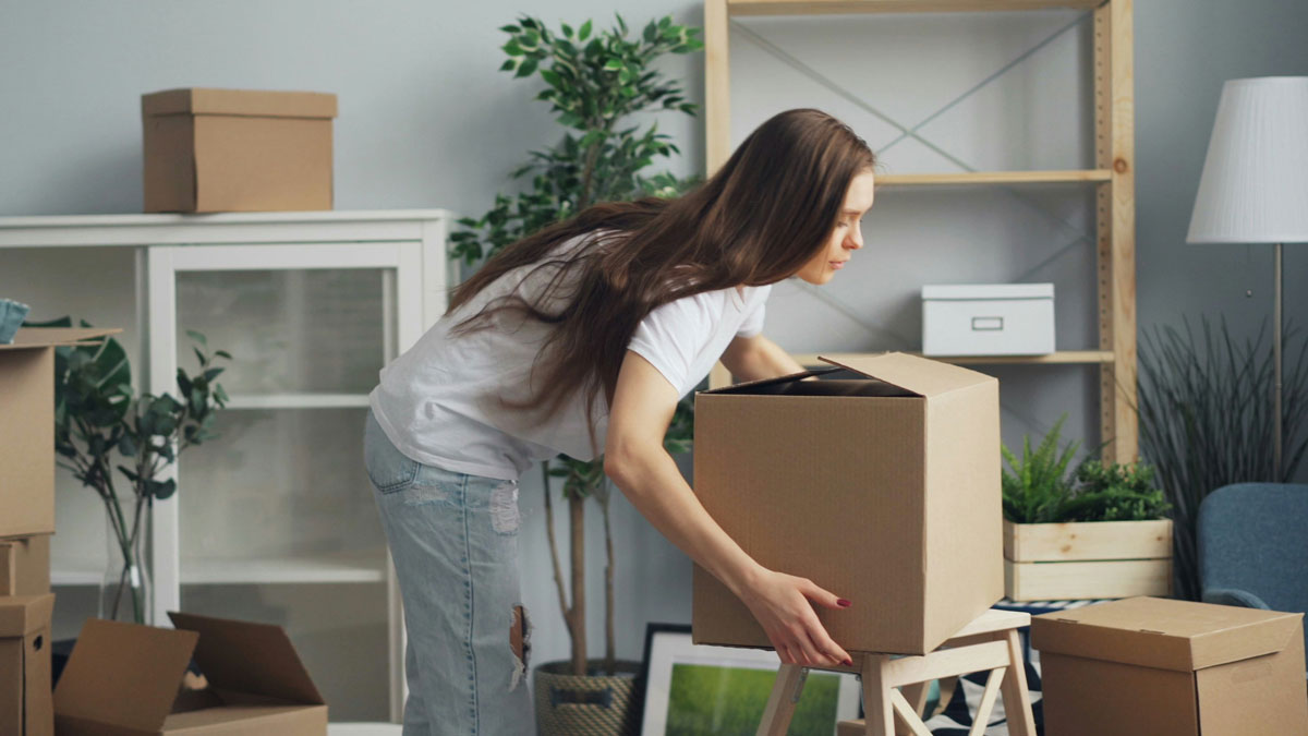 Woman packing a box indoors, reflecting hesitation after last attempt to share important news with dad.