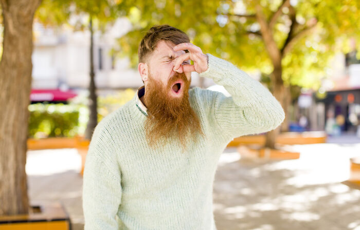 Bearded man outdoors holding nose with eyes closed, illustrating deaf people revealing surprisingly silent things.