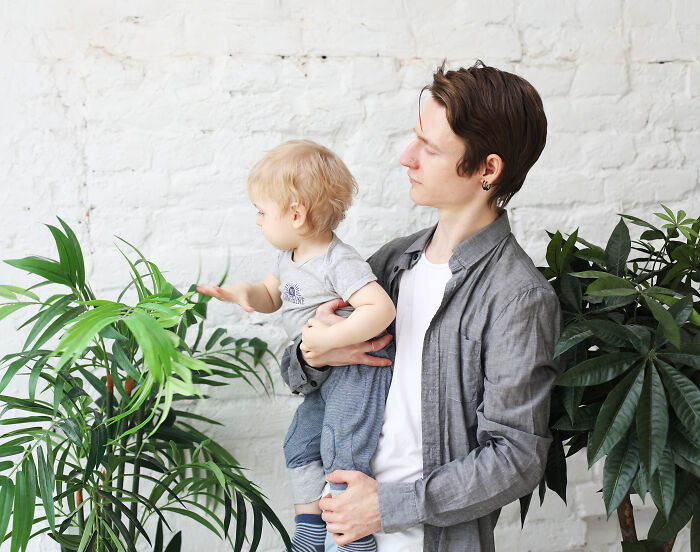 Young man holding a child near green plants, illustrating deaf people revealing surprisingly silent things assumed noisy.