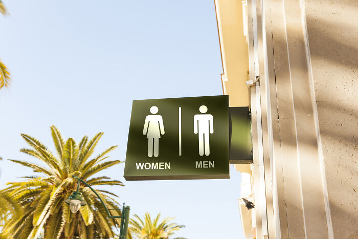 Restroom sign outdoors with palm trees in the background, relating to deaf people and surprisingly silent things.