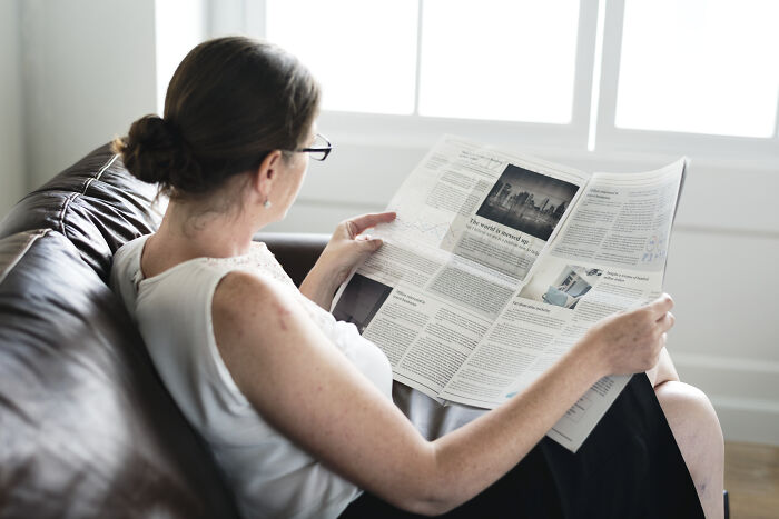 Woman reading newspaper quietly on a couch, highlighting deaf people’s perspective on surprisingly silent things and experiences.