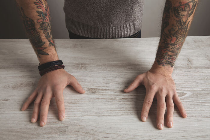 Person with tattooed arms resting hands on a wooden table illustrating deaf people’s perspective on silent things.