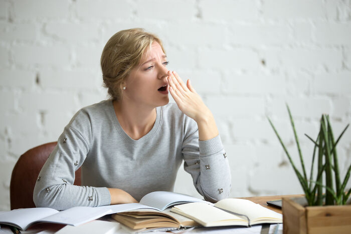 Young woman yawning quietly while reading books, illustrating deaf people's perspective on surprisingly silent things.
