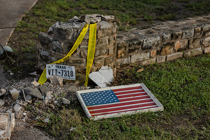 Damaged stone wall with Texas license plate and fallen American flag, marked with caution tape after flood disaster. Damaged stone wall with Texas license plate and fallen American flag, marked with caution tape after flood disaster.