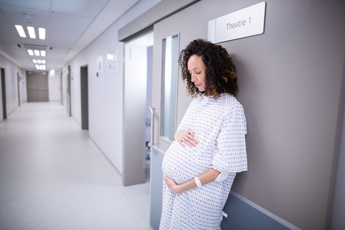 Pregnant woman in delivery room hallway, preparing for birth, relating to delivery room baby DNA testing process.