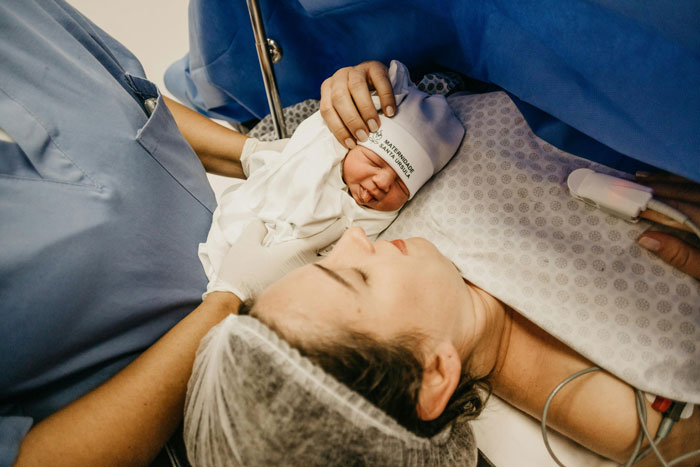 Newborn baby held gently by medical staff in delivery room, highlighting the moment of baby DNA and birth connection.
