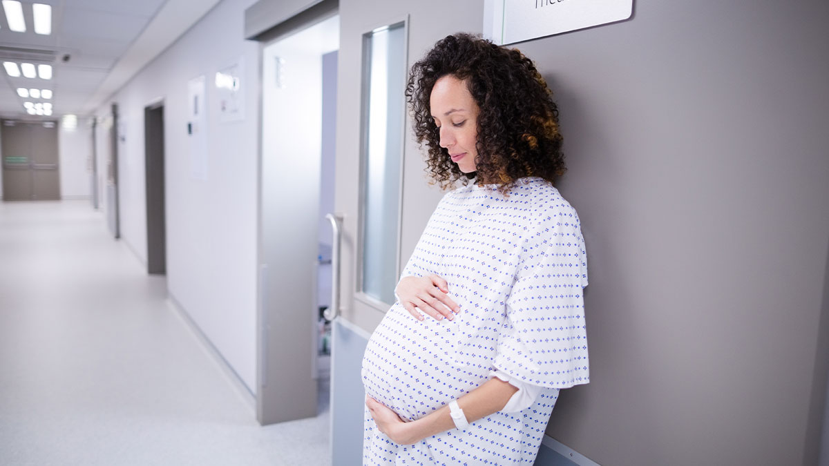 Pregnant woman in hospital gown standing in hallway, reflecting on MIL's jokes questioning baby's paternity issue.