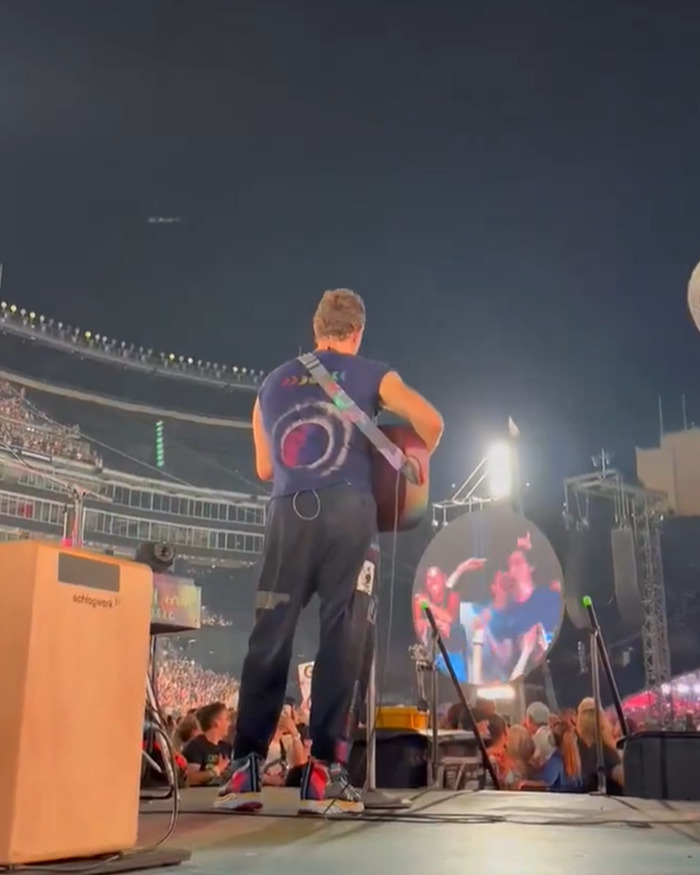 Musician performing on stage at a large concert venue with a crowd and Kiss Cam screen in the background. Musician performing on stage at a large concert venue with a crowd and Kiss Cam screen in the background.