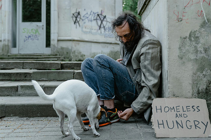 Homeless man sitting on city steps with a dog and a sign, illustrating moments people decided to stop helping others.