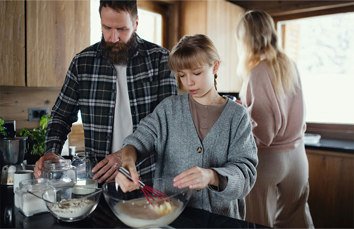 A family in a kitchen with a child mixing ingredients while an adult watches, reflecting moments people decided to stop helping others.