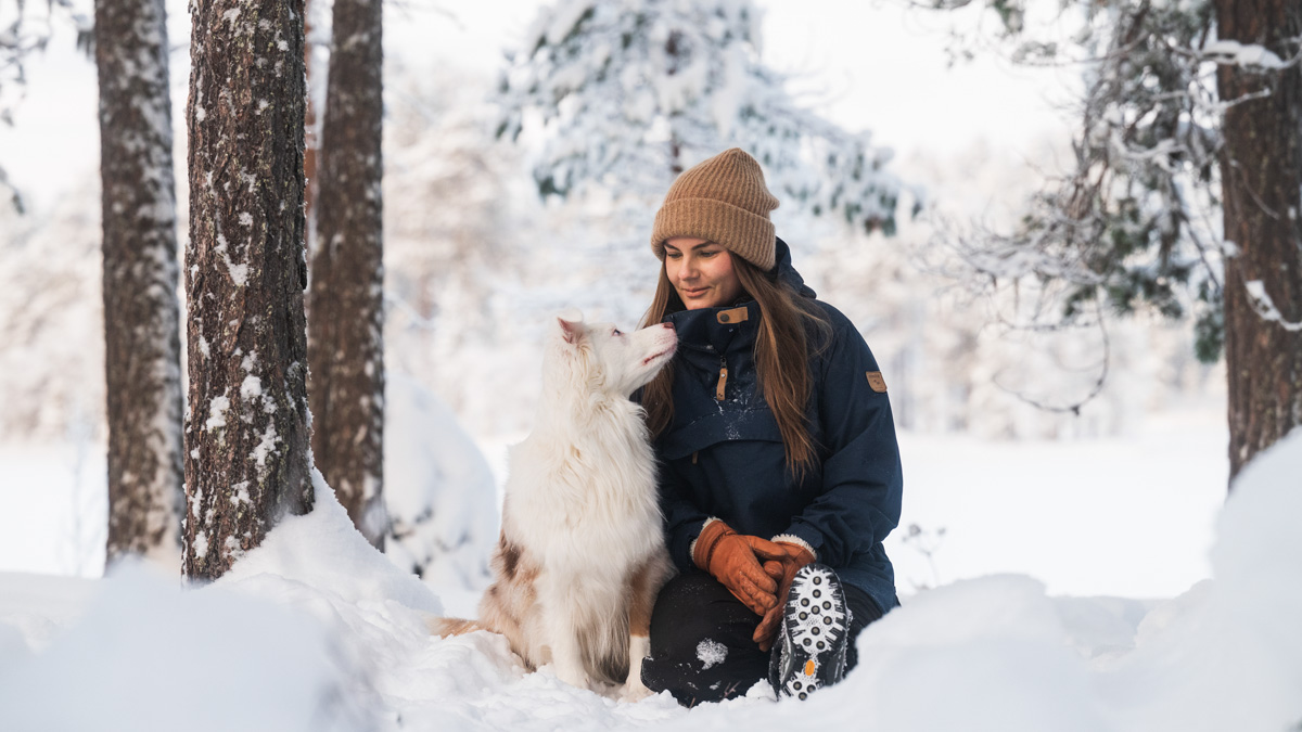 Woman sitting in the snow with her dog in a winter forest, embracing cabin in the woods lifestyle and nature living.