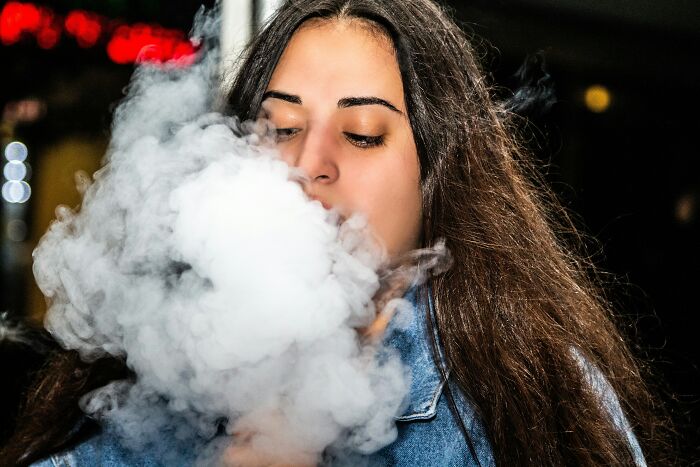 Young woman blowing a large cloud of smoke in public, illustrating wild and disgusting things people did in public.