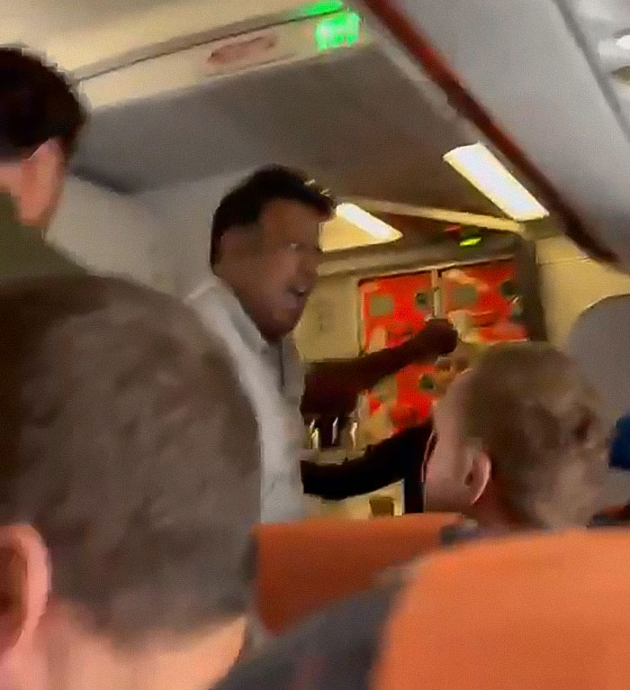 Man threatening to explode plane mid-flight, with passengers reacting inside an airplane cabin during a tense moment. Man threatening to explode plane mid-flight, with passengers reacting inside an airplane cabin during a tense moment.