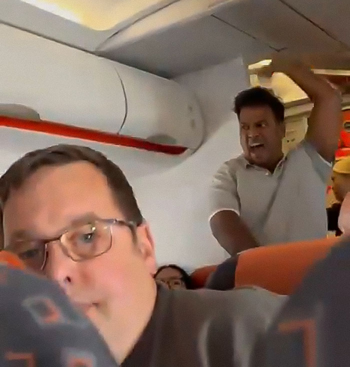 Man threatens to explode plane mid-flight shouting aggressively while passengers prepare to tackle him on an airplane. Man threatens to explode plane mid-flight shouting aggressively while passengers prepare to tackle him on an airplane.