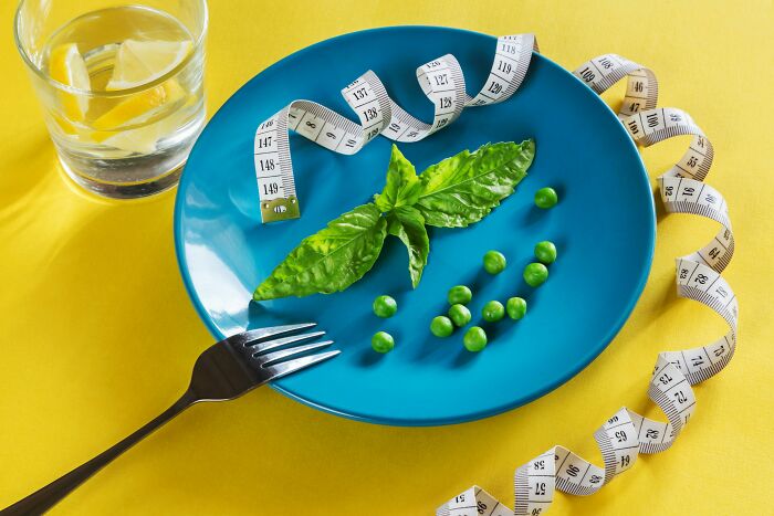 Blue plate with basil and peas, measuring tape wrapped around, fork nearby, and a glass of water, illustrating bizarre beliefs.