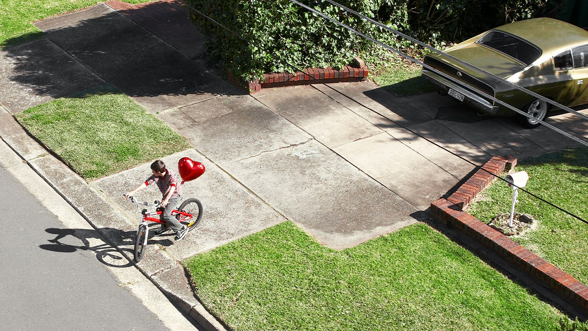 Child riding bike on neighboru2019s driveway with a red heart-shaped balloon, illustrating parents treating it like their own backyard.