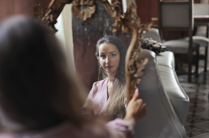Young woman looking at her reflection in a mirror, representing escape room employees stories and personal experiences.
