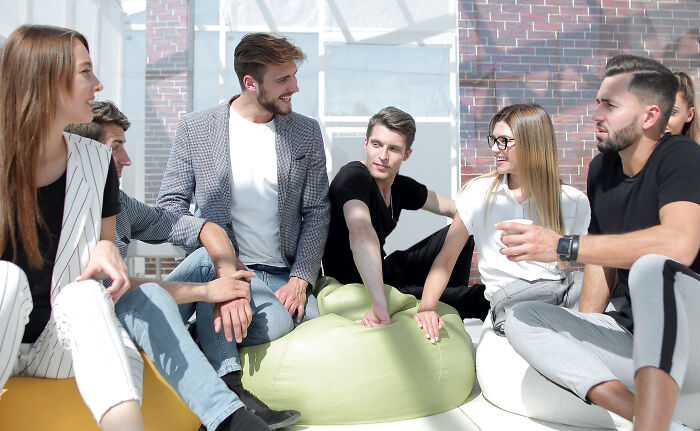 Group of escape room employees sharing stories and experiences in a bright, casual meeting setting with relaxed seating.