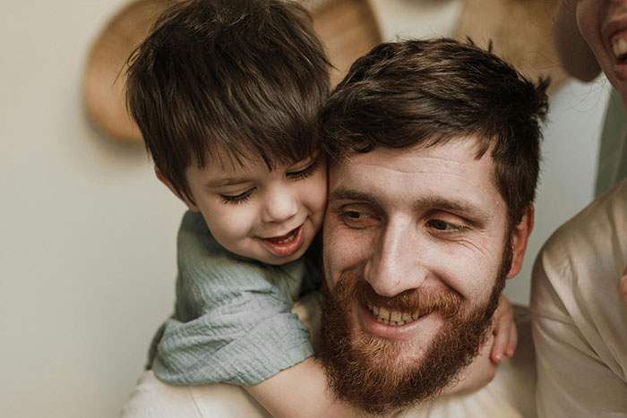 Bearded man smiling while young boy hugs him from behind, highlighting co-parenting and secret child themes. Bearded man smiling while young boy hugs him from behind, highlighting co-parenting and secret child themes.