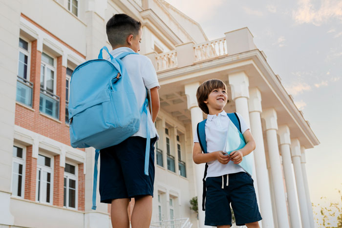Two boys with backpacks standing outside a school building, illustrating a stepkid and bathroom refusal situation. Two boys with backpacks standing outside a school building, illustrating a stepkid and bathroom refusal situation.
