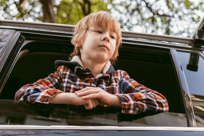 Young boy leaning out of car window, looking pensive, illustrating stepkid suspicion in family disputes. Young boy leaning out of car window, looking pensive, illustrating stepkid suspicion in family disputes.