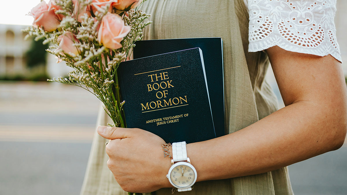 Person holding the Book of Mormon and a bouquet of flowers symbolizing people raised Mormon discussing cult questions.