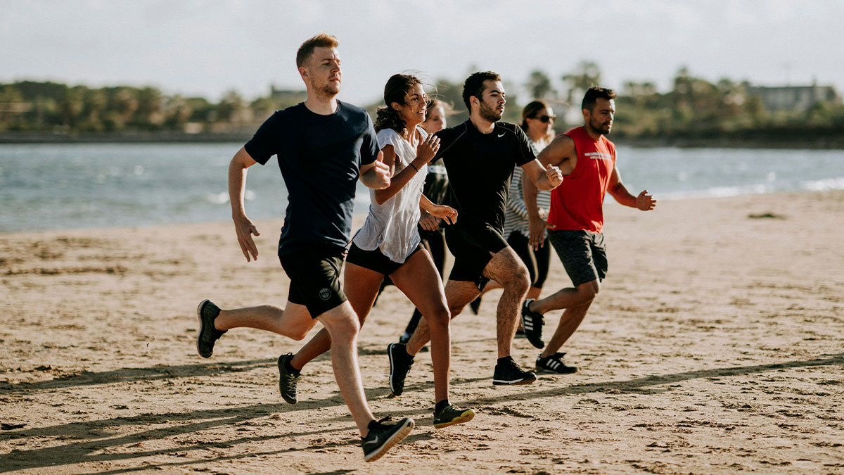 Group of young adults running on the beach as a healthy exercise to avoid effects of death machines on the body