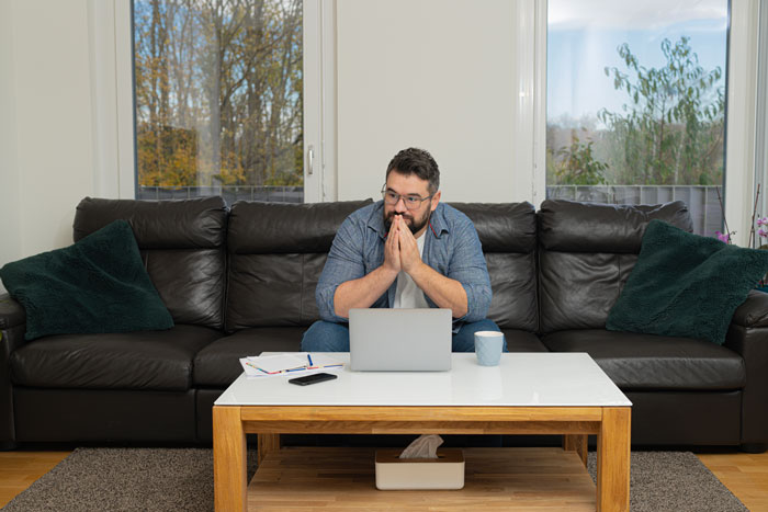 Man sitting on a couch with laptop, looking worried and thoughtful in a home setting, reflecting on false accusation wife father.