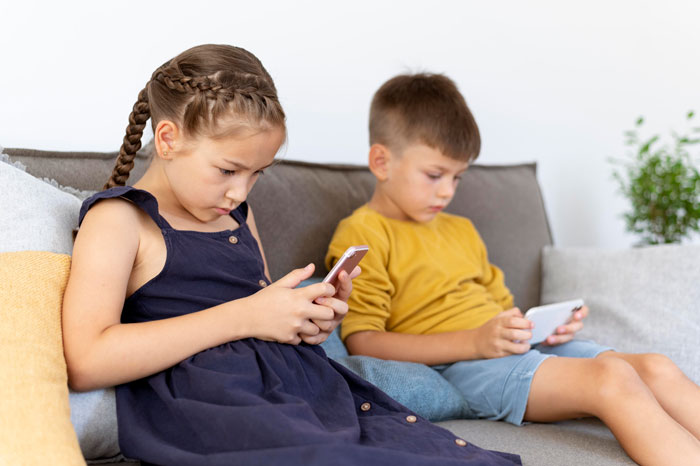 Two children sitting on a couch focused on their phones, symbolizing tension from false accusation involving wife and father.
