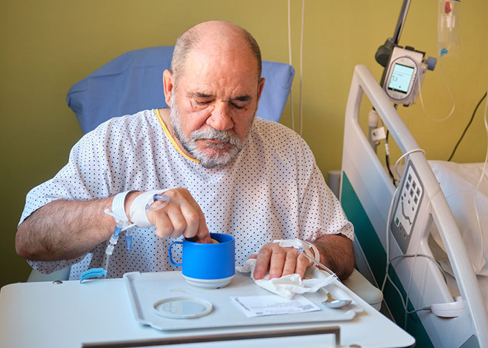 Elderly man in hospital gown with IV, sitting in bed and drinking from a blue cup, representing organ donation refusal. Elderly man in hospital gown with IV, sitting in bed and drinking from a blue cup, representing organ donation refusal.