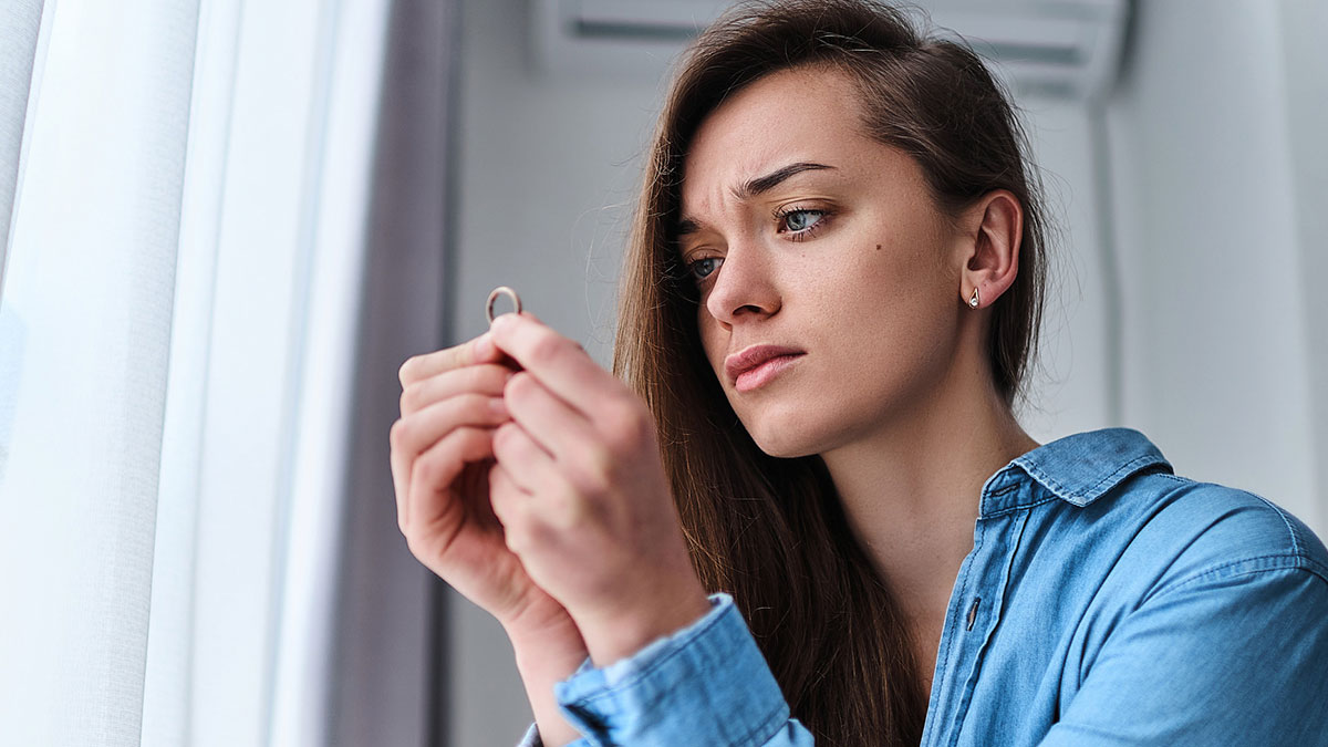 Young woman holding a ring, looking upset and thoughtful after fiancu00e9u2019s family publicly calls her trial wife and warm-up.