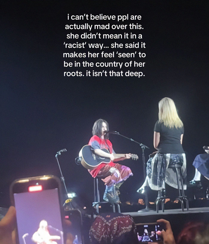 Billie Eilish performing on stage with a guitar during a concert amid controversy over a comment deemed racist. Billie Eilish performing on stage with a guitar during a concert amid controversy over a comment deemed racist.