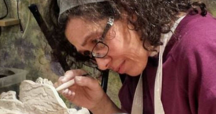 Artist with curly hair and glasses creating a detailed visual story sculpture symbolizing struggle and strength.