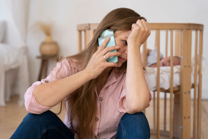 Stressed woman talking on phone near baby crib, upset about grandpa skipping babysitting duty for party weekend. Stressed woman talking on phone near baby crib, upset about grandpa skipping babysitting duty for party weekend.