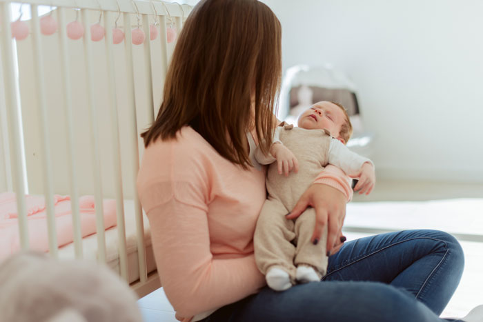 Woman sitting on the floor holding a sleeping baby near a crib, illustrating grandpa skipping babysitting duty and family tension. Woman sitting on the floor holding a sleeping baby near a crib, illustrating grandpa skipping babysitting duty and family tension.