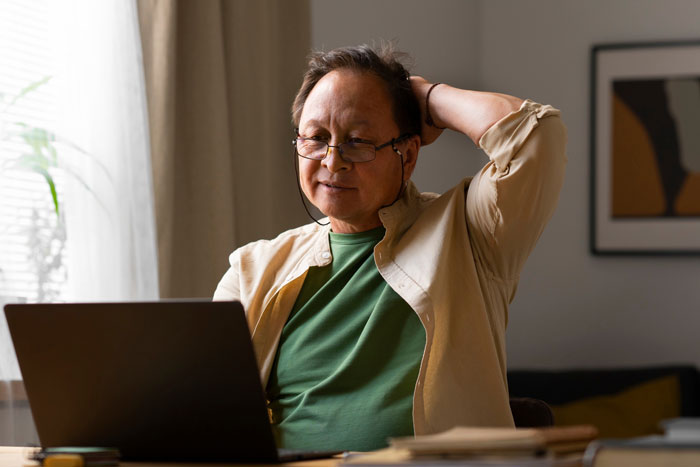 Grandpa using laptop at home, looking frustrated as he skips babysitting duty for party weekend plans. Grandpa using laptop at home, looking frustrated as he skips babysitting duty for party weekend plans.