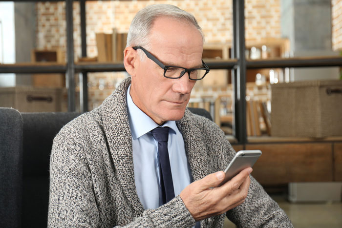 Older man in glasses wearing a sweater and tie, looking at smartphone, reflecting grandpa skipping babysitting duty for party weekend. Older man in glasses wearing a sweater and tie, looking at smartphone, reflecting grandpa skipping babysitting duty for party weekend.